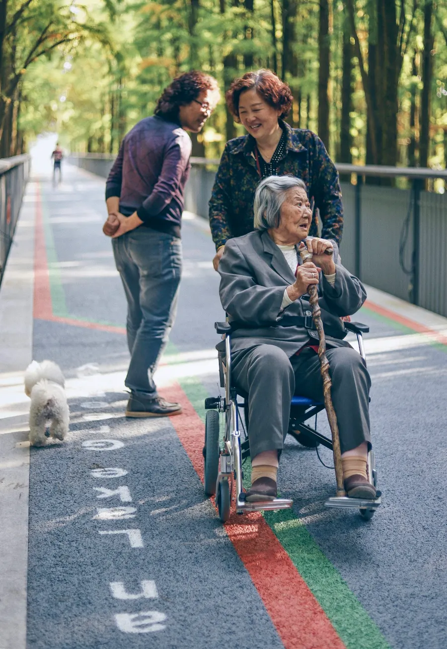 Caregivers walking with an older woman in a wheelchair
