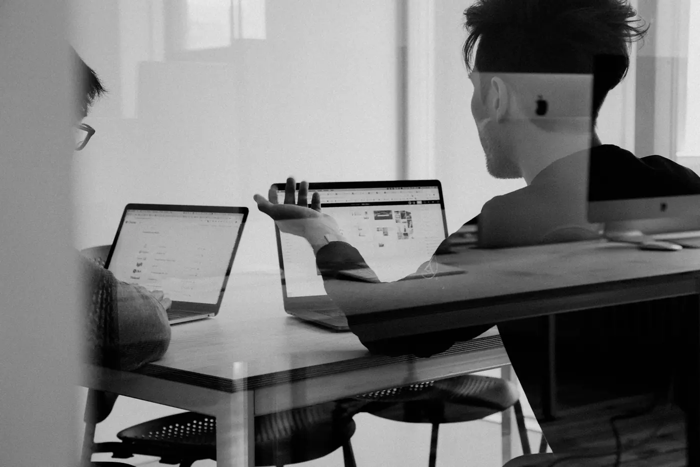 Two colleagues working through a problem together on laptops at a shared desk